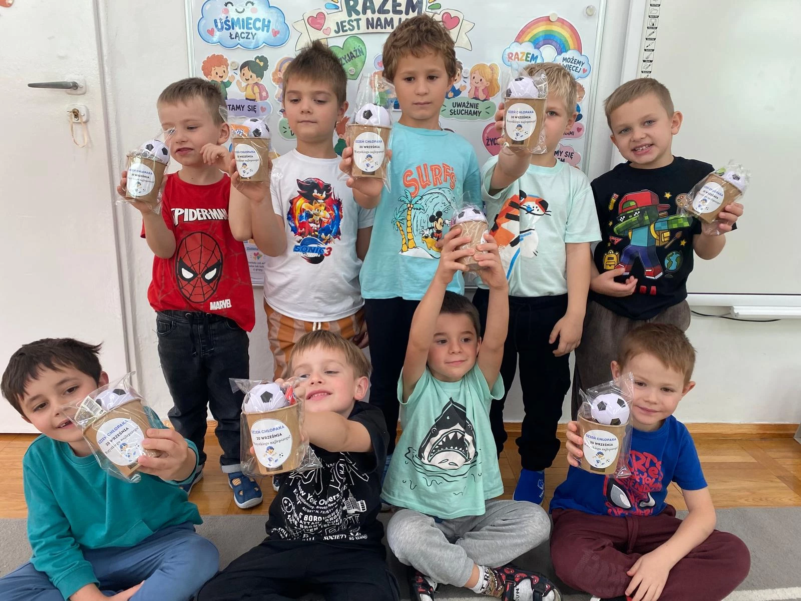 Dziesięciu chłopców trzyma upominki z okazji Dnia Chłopaka.